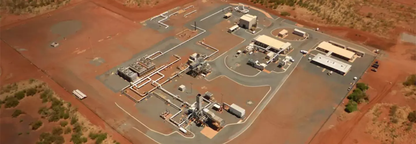 An industrial plant sits surrounded by red, barren land, its complex structure of buildings and machinery neatly organized within a clearly demarcated area.