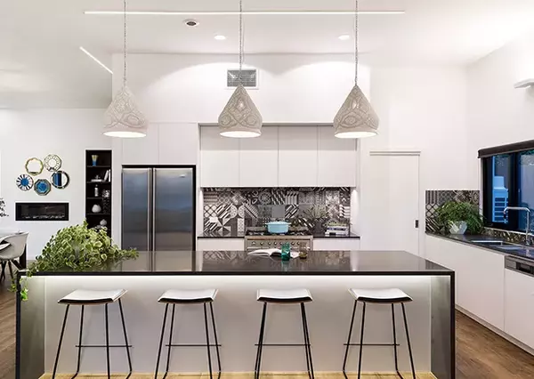 A modern kitchen features sleek appliances and a large island with bar stools, illuminated by pendant lights, in a spacious, well-lit home interior.