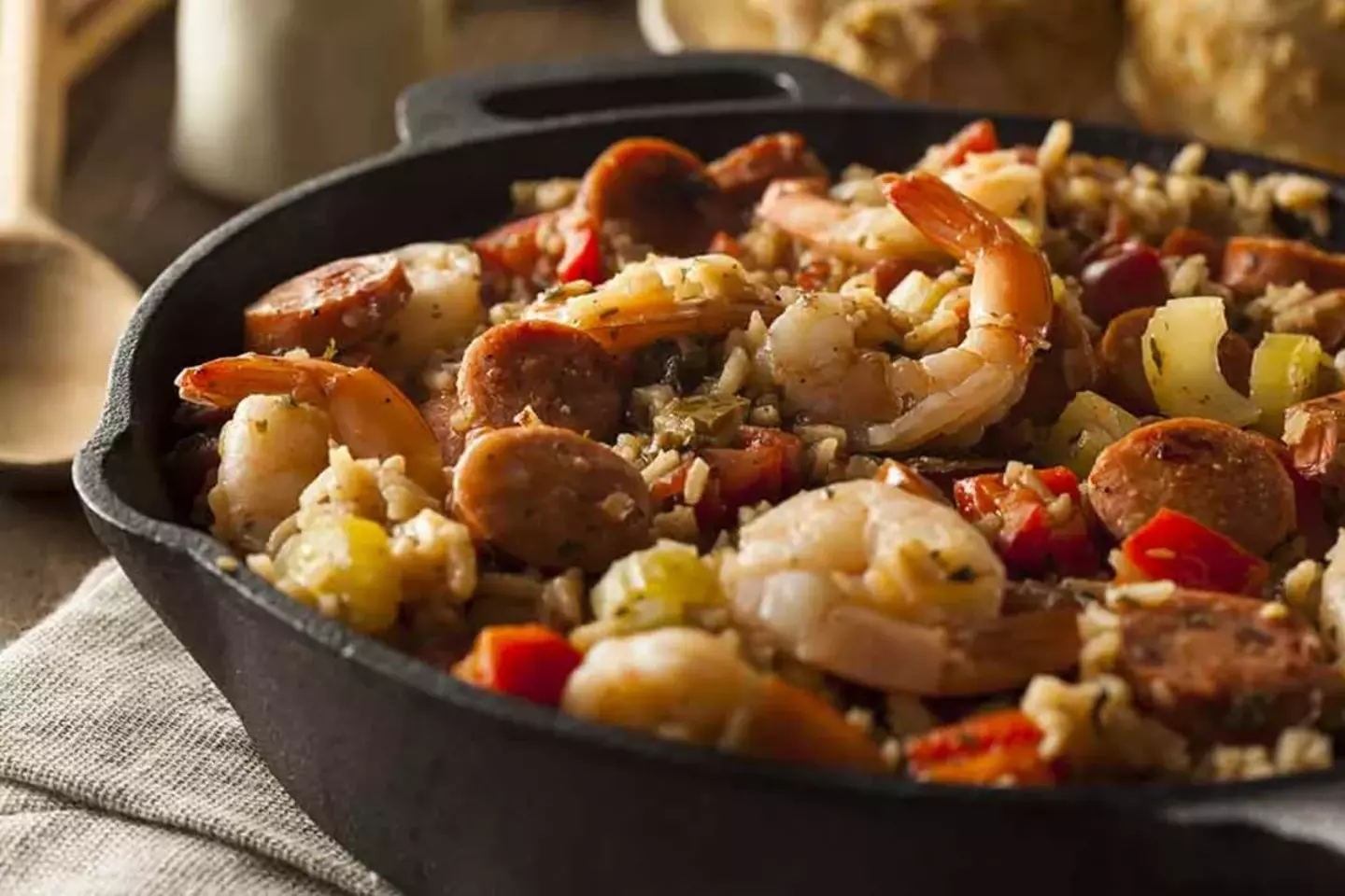 A skillet contains a hearty mixture of shrimp and diced sausage, mingled with chopped vegetables like peppers and onions, suggesting a flavorful meal, presented on a rustic wooden table.