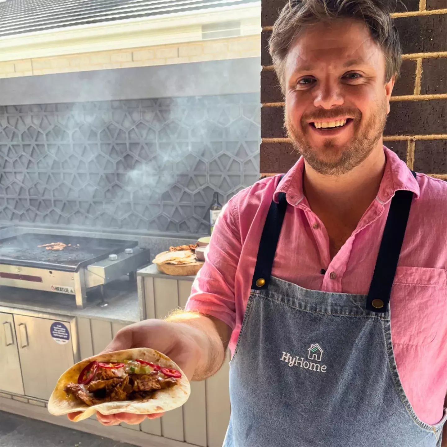 Smiling chef Michael Weldon preparing food in an outdoor kitchen using a gas BBQ.