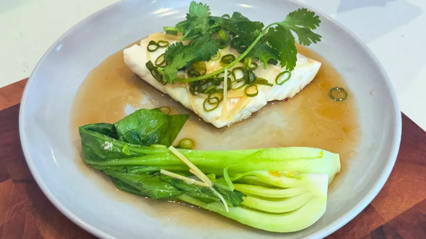 Steamed fish fillet with bok choy and sauce, served on a white plate.