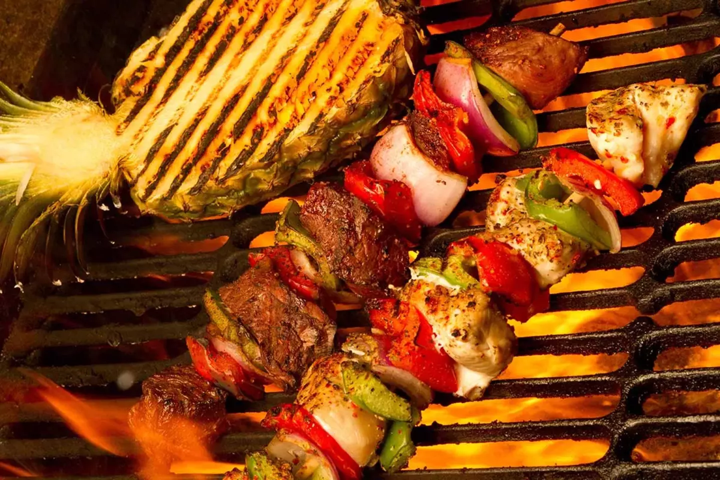 Various foods including corn, meat, and skewered vegetables are grilling over an open flame, showcasing a vibrant display of cooking on a barbecue.