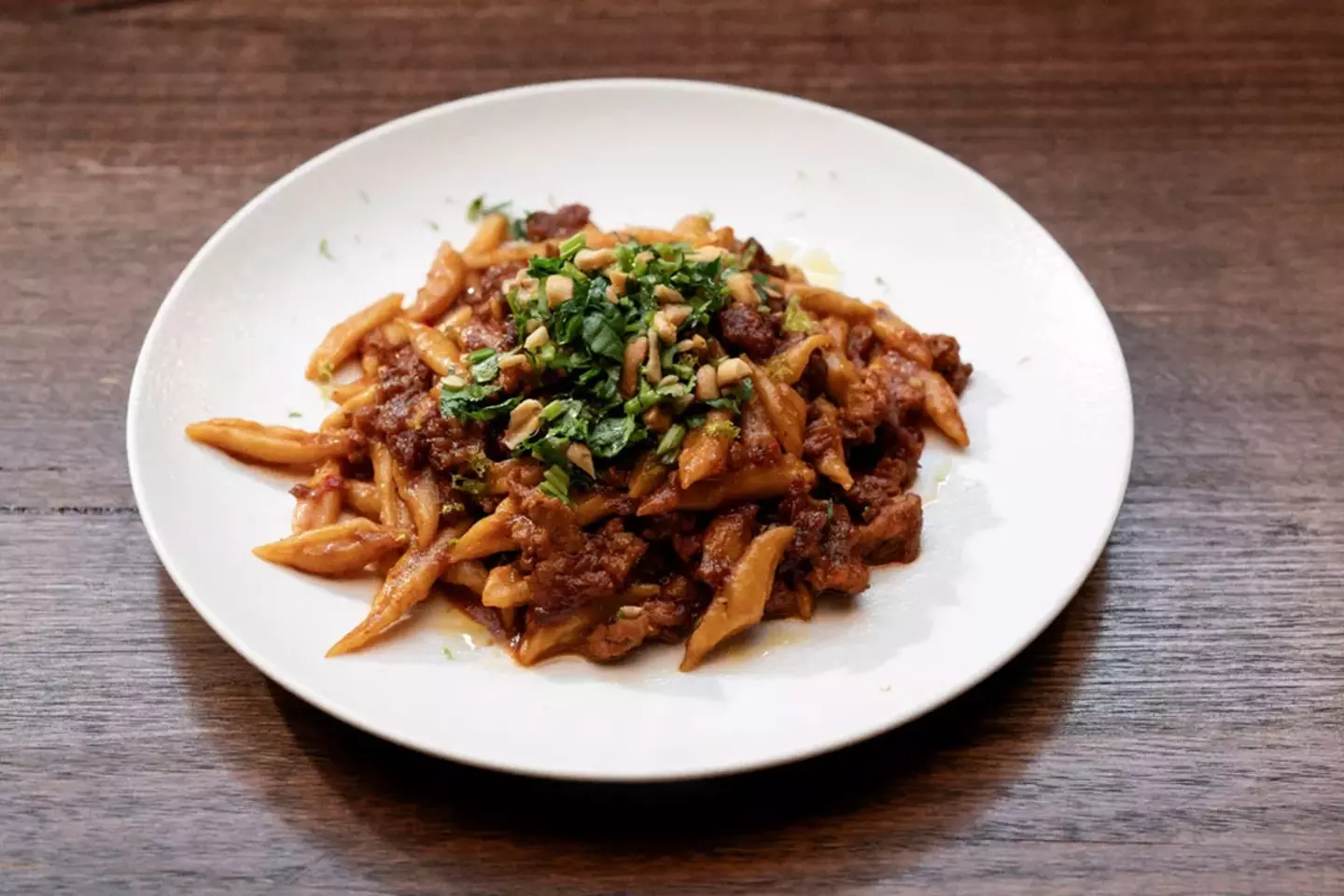 Stir-fried scissor cut noodles dish with meat, vegetables, and sauce on a white plate.