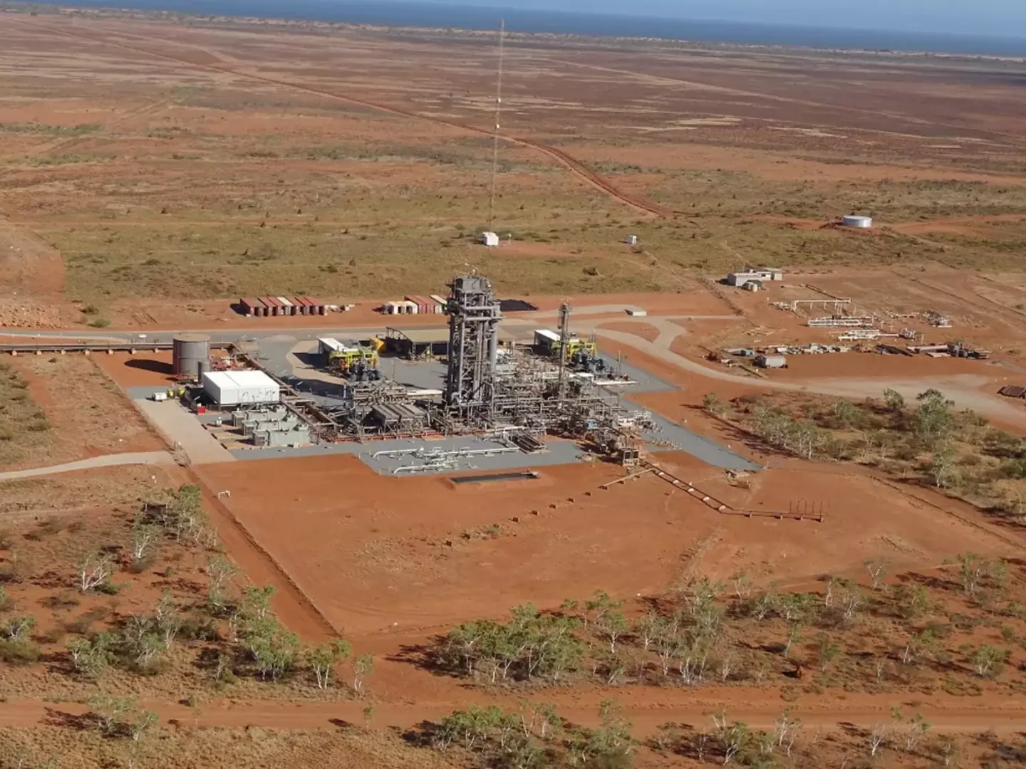 An industrial facility with complex machinery sits amidst a vast, arid landscape, indicating an extraction or processing site likely for minerals or oil.