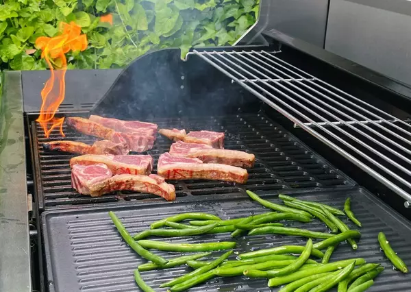 Close-up of steaks and vegetables being grilled on a gas BBQ.