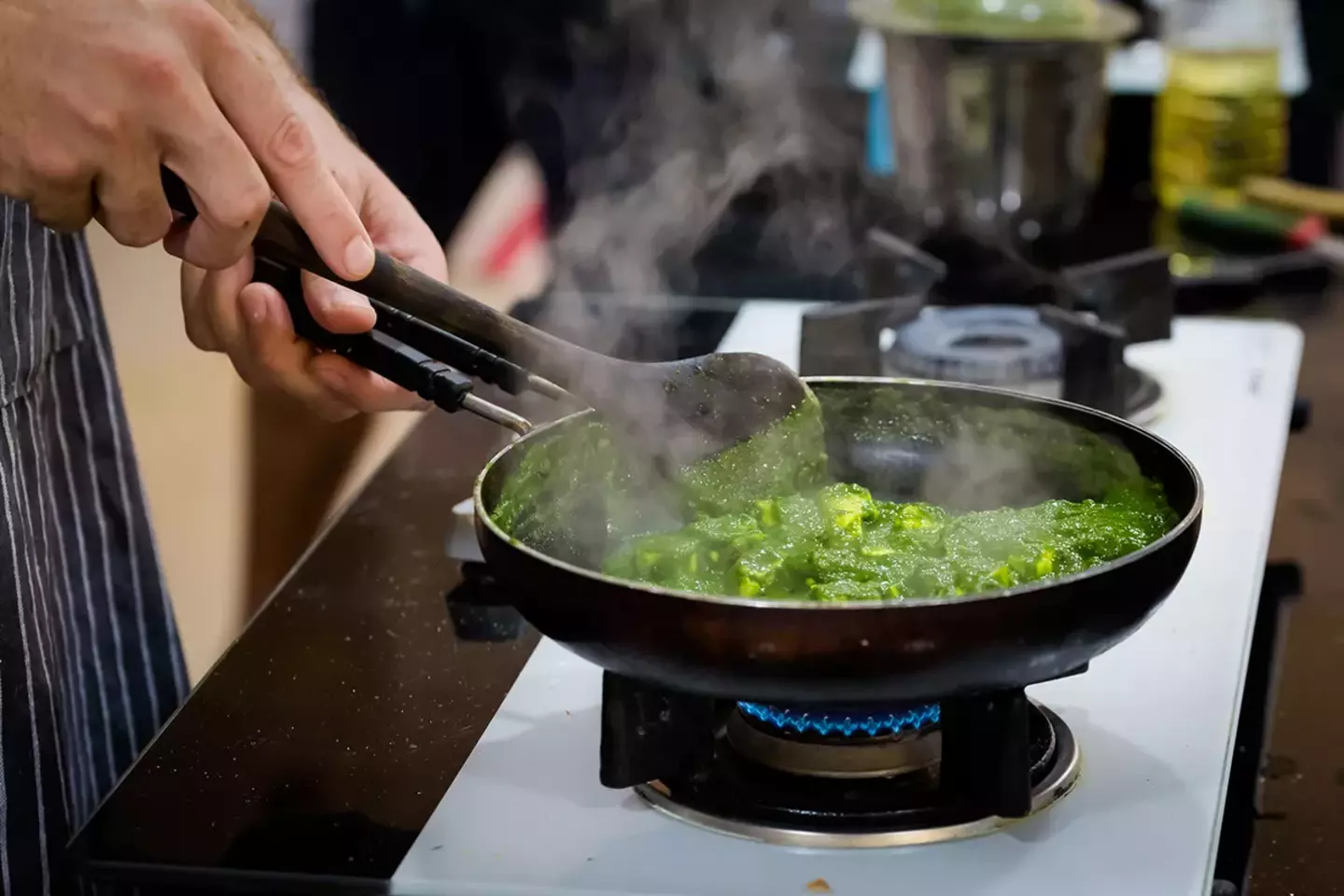 Person cooking vegetables in a wok on a gas stovetop flame.