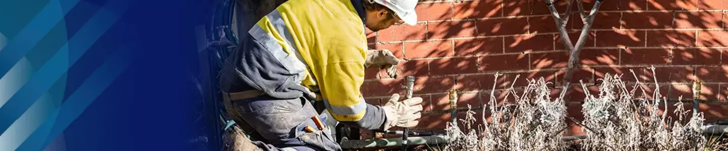 Gas technician in safety gear working on an outdoor residential gas connection.