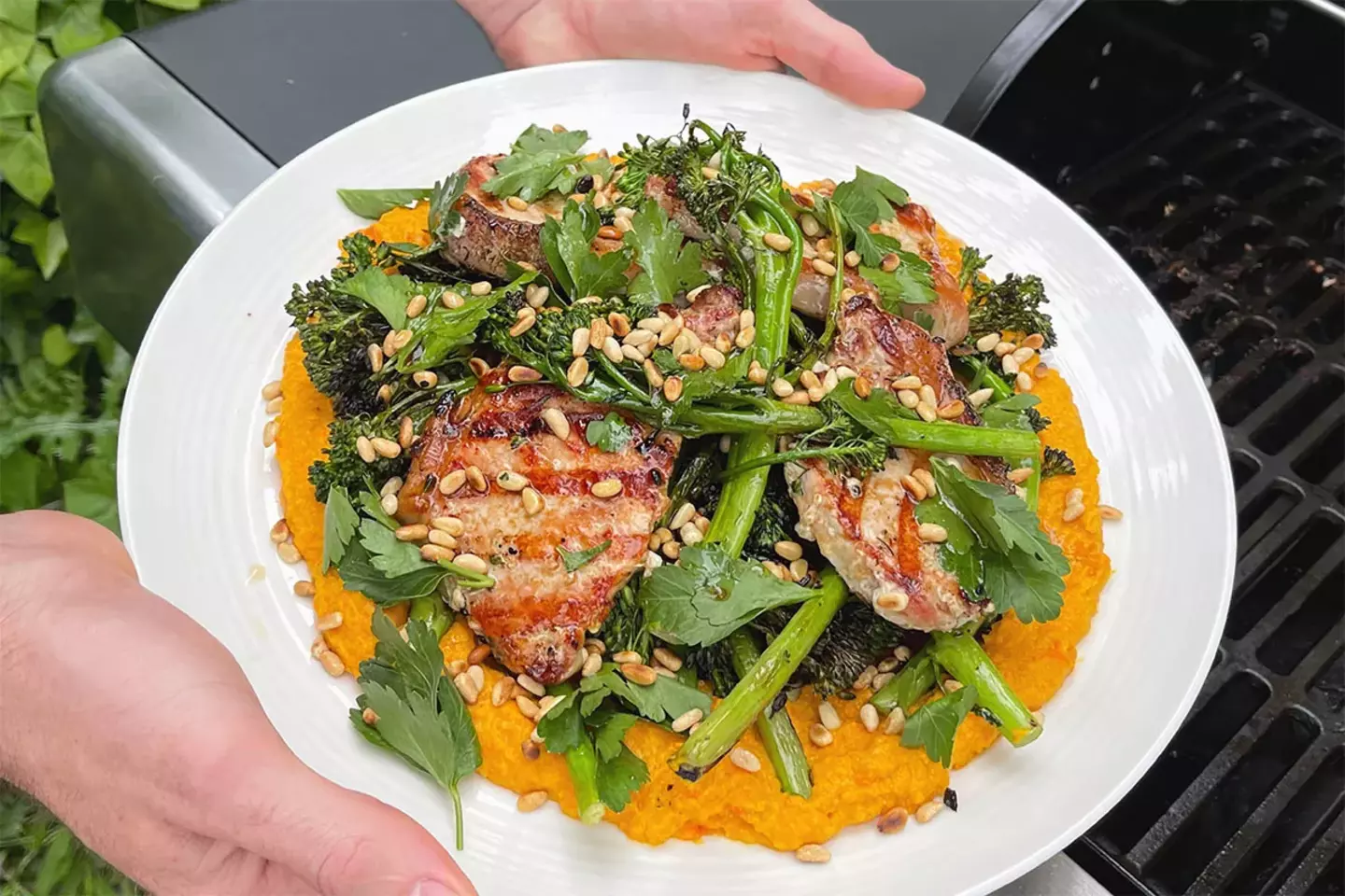 Fresh salad topped with grilled pork and vegetables, served in an outdoor dining setting.
