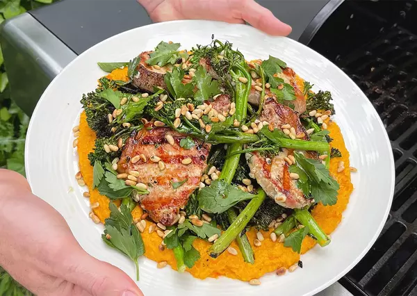 Fresh salad topped with grilled pork and vegetables, served in an outdoor dining setting.