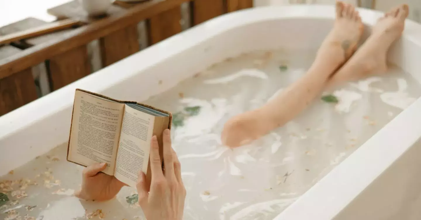 A woman relaxing in a hot bath, reading a book with her feet propped up.