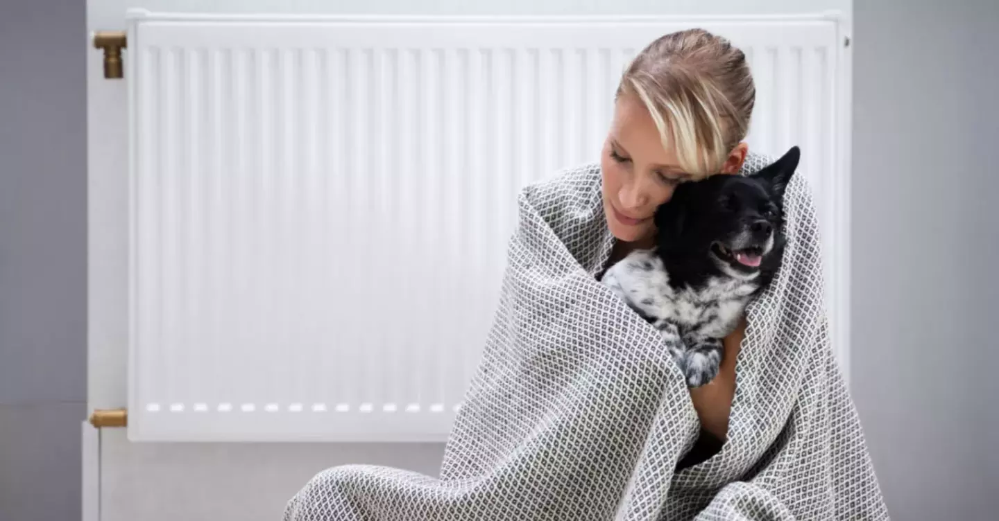A woman and her dog wrapped in a blanket, warming up by the gas heater.